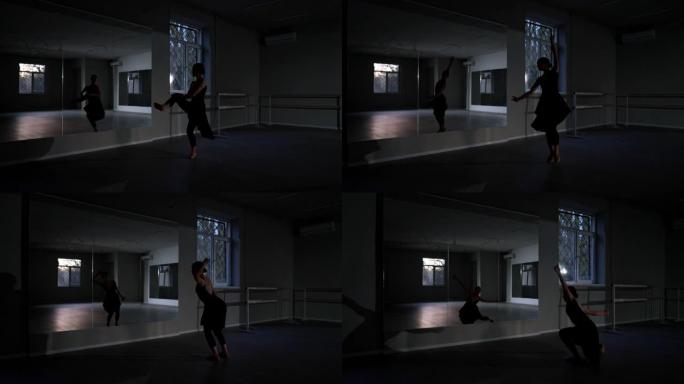在黑暗中的舞蹈工作室的镜子前排练的苗条芭蕾舞演员的宽镜头充满活力的艺术舞蹈。才华横溢的白人年轻女子跳