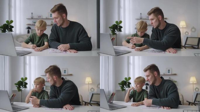 一位年轻的父亲帮助他7岁的儿子坐在客厅的桌子旁做作业。