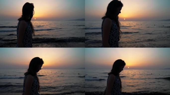 一个女人在海滩上散步的剪影。欣赏日落