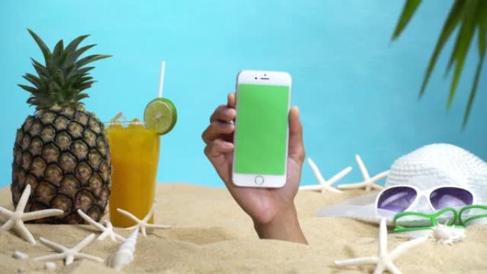手握着一部绿屏智能手机穿过沙滩。用于在智能手机上创建媒体。