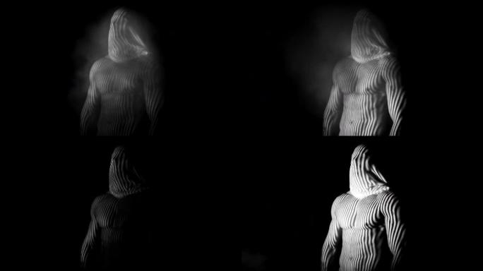 灰色肌肉男子与面纱的脸摆姿势的相机与抽象的照明效果与黑色背景的烟雾效果