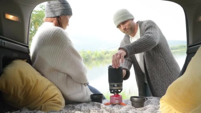 4k女人和男朋友坐在便携式炉灶上通用汽车煮茶的开放式行李箱中