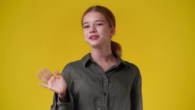一个女孩在黄色背景上挥手打招呼的4k慢动作视频。