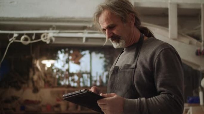 高级男雕塑家在他的工作室里看着平板电脑