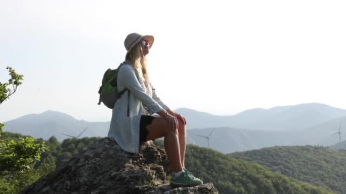 女徒步旅行者到达绿山风力涡轮机上方的岩石山顶