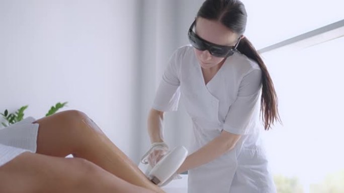 美容师医生在迷人的年轻女性腿上做elos脱毛。女人的腿得到激光脉冲破坏毛囊。激光脱毛程序美容师沙龙。