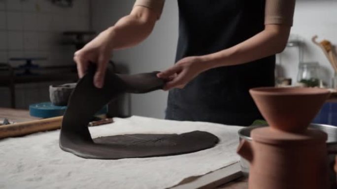 匿名年轻女子在陶艺工作室用美工刀模制粘土。波特女孩把粘土模制成盘子。教育、商业、艺术天赋和创意手工制