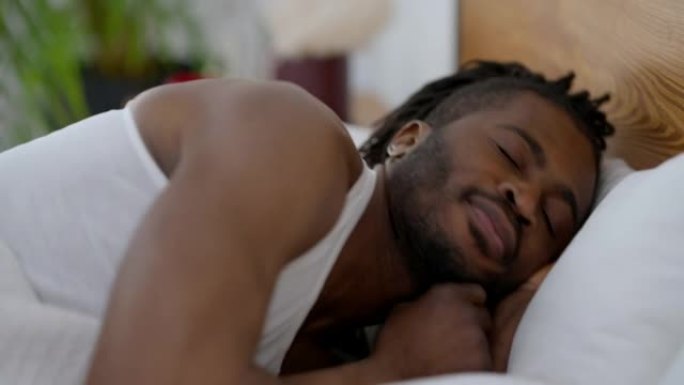 熟睡的非洲裔美国男子翻身躺在家里的床上。室内卧室里快乐帅哥的肖像。放松和休闲概念。