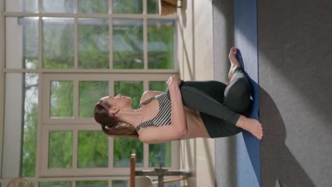女运动员用笔记本电脑在瑜伽垫上做脊柱扭转。家庭锻炼。纺纱效果