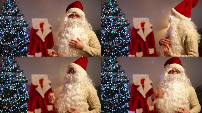 微笑的男人戴着白胡子眼镜和新年帽子，回头看着圣诞老人外套，转身看着相机打手势。圣诞节积极自信的年轻人