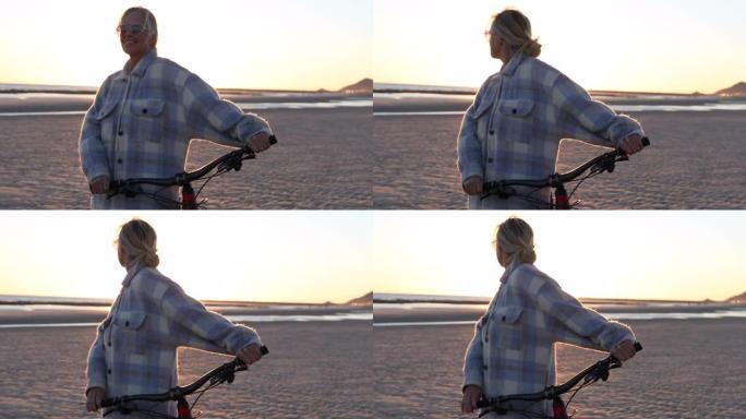 女骑自行车的人从海滩观看日出，然后出发