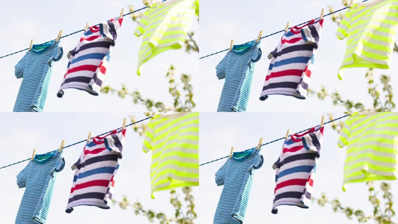 洗衣日在户外用绳子清洗衣服。彩色t恤挂在蓝天下的洗衣线上
