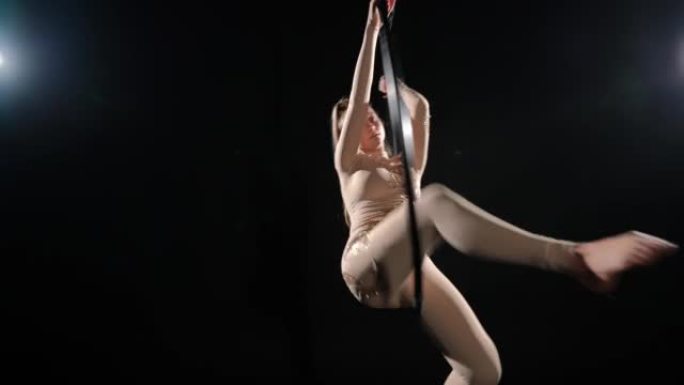 自信苗条的女人在黑色背景的空气箍上表演，背光。灵活的高加索空中体操运动员在舞台上弯曲分裂的飞行舞蹈。
