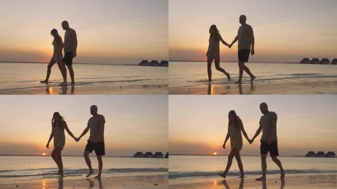 手牵手的夫妇。日落海滩上紫色和橙色天空的深色轮廓。