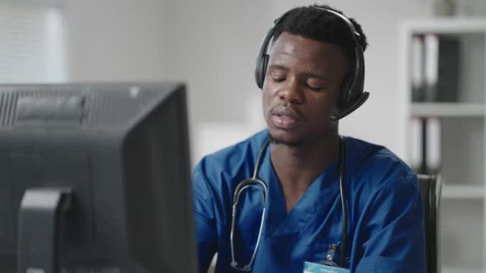一个黑人穿着医生的制服坐在电脑旁，一边用耳机接听电话，一边写病人的卡。救护车热线接听电话并分发救护车