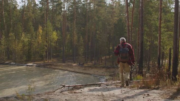 孤独的中年男子正在用池塘探索森林，秋天独自行走，享受好天气