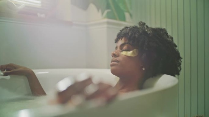美丽的非洲民族妇女在现代浴室放松。佩戴保湿凝胶眼罩冥想