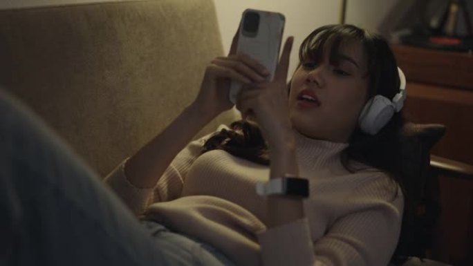 年轻女子在家使用手机在耳机上听音乐