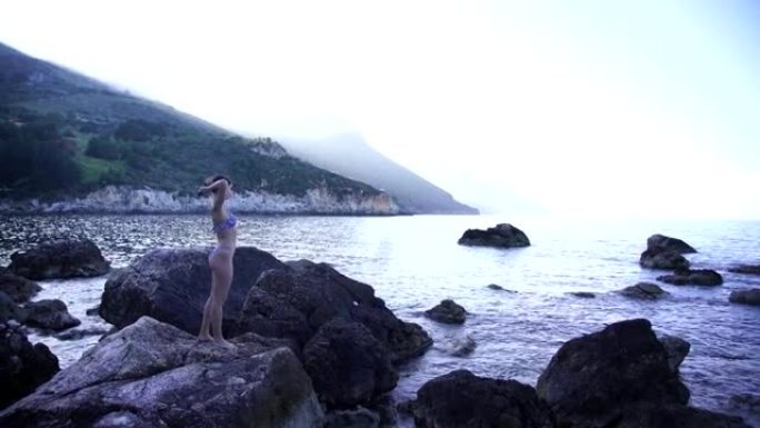 穿着泳装的年轻女子站在海洋附近的一块岩石上
