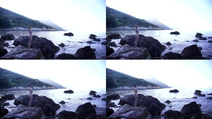 穿着泳装的年轻女子站在海洋附近的一块岩石上