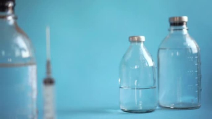 疫苗接种概念，注射器和烧杯用盐水特写，手用蓝色手套放在玻璃小瓶上注射药物，蓝色背景。横向视频复制空间