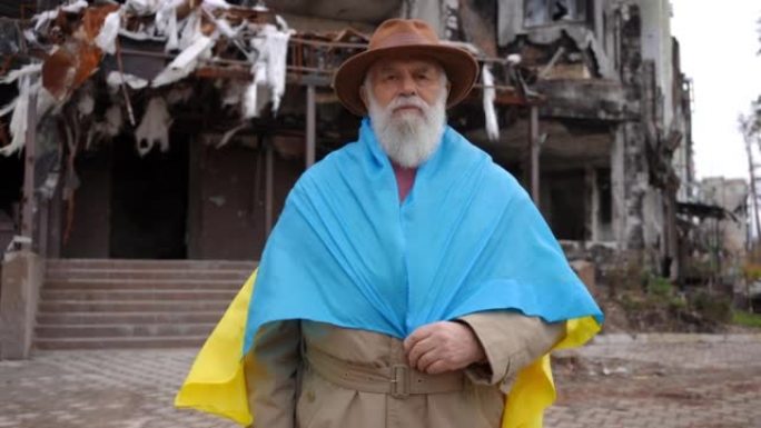 高级绝望男子的肖像，看着站在乌克兰被毁城市被毁的被炸毁的民用建筑背景下的相机。悲伤无助的退休人员在户
