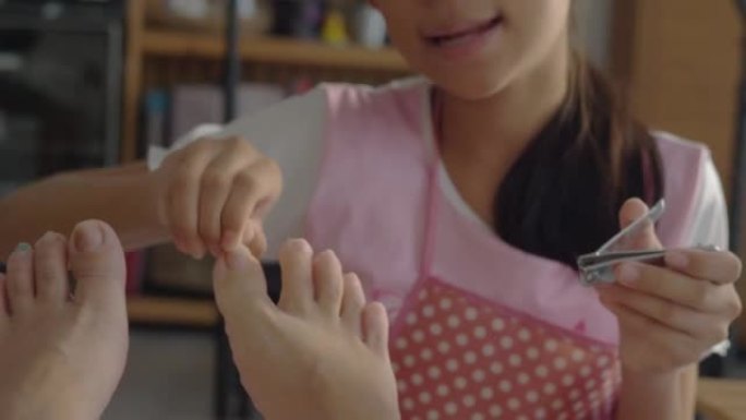 亚洲女孩在家里用指甲锉把母亲的指甲脚趾涂在地板上，周末概念水疗。