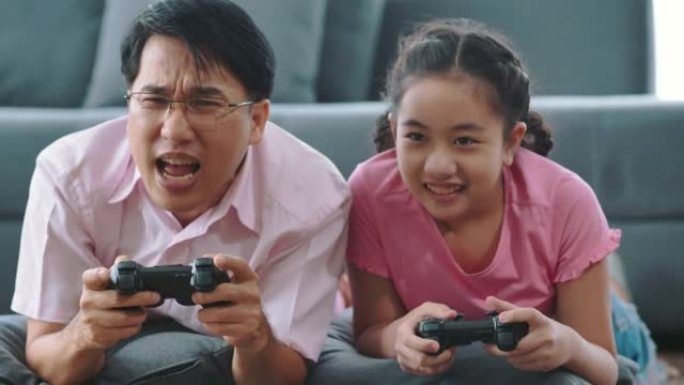女孩和她的父亲用游戏手柄玩控制台电脑游戏，在家玩得开心