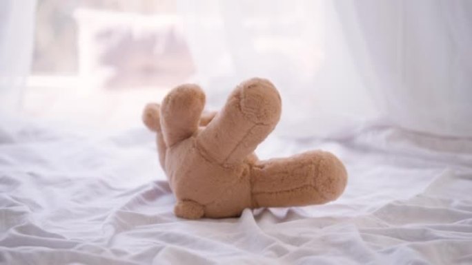 特写棕色泰迪熊躺在室内的床上。晴天卧室里的玩具在白色床单上。童年的概念。