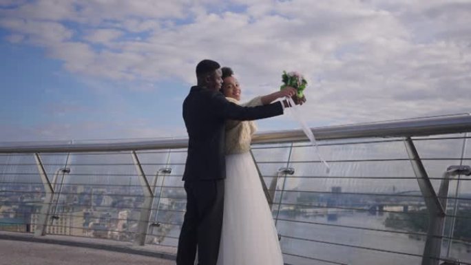 实时摄像机放大到快乐微笑的非洲裔美国新婚夫妇，模仿桥上的泰坦尼克号场景。激动的爱心新娘和新郎在户外结