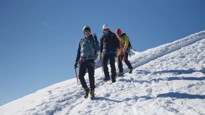 一队登山者沿着陡峭的山峰移动。对着镜头微笑