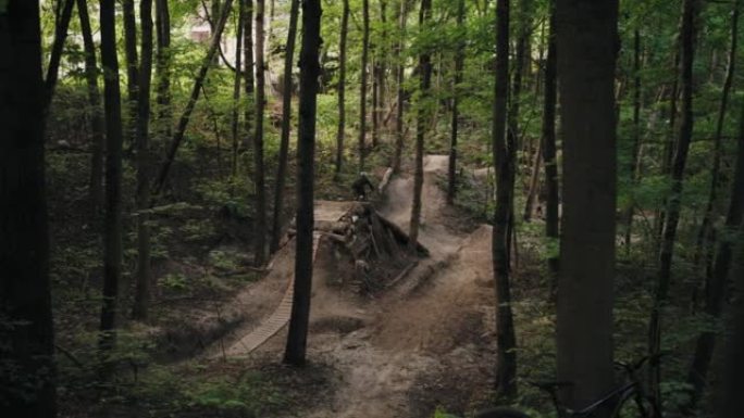 一名在森林中的MTB上戴着头盔的男子加速并跳到森林跑道上的巨大跳板上。骑自行车的人跳上跳板，降低了山