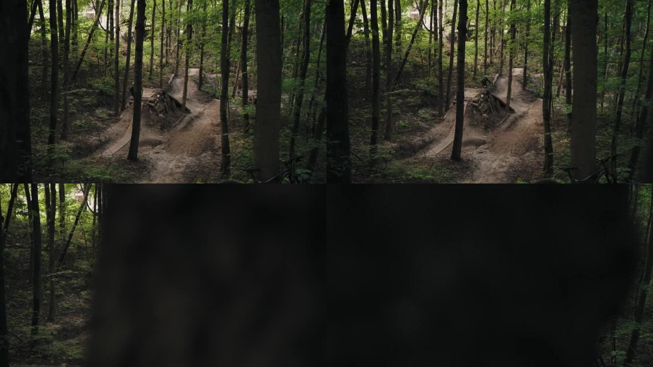 一名在森林中的MTB上戴着头盔的男子加速并跳到森林跑道上的巨大跳板上。骑自行车的人跳上跳板，降低了山