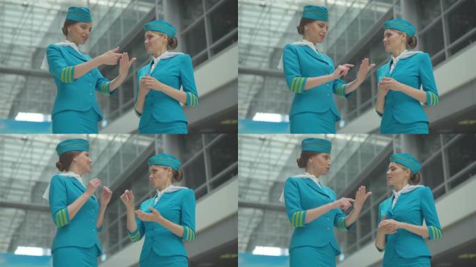 激动的美丽空姐向机场的年轻同事解释新技术设备的工作。白种人女性出发前谈话的角度底视图。快乐空姐的肖像
