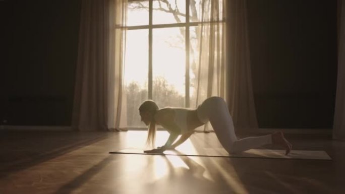 一位穿着白色运动服的年轻女子正伸展着一个大大厅，大厅里有大窗户，以慢动作的方式，阳光透过窗户。