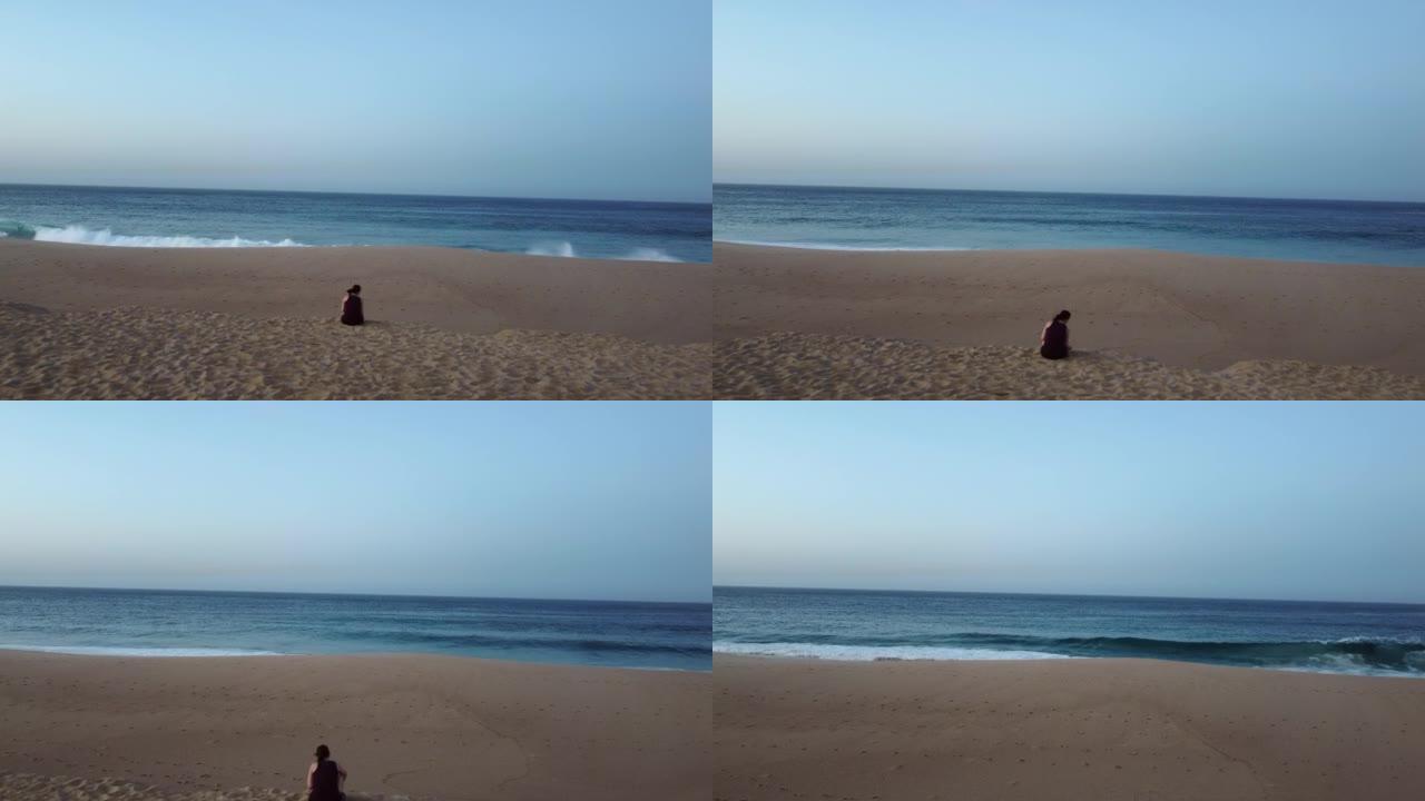 空中无人机拍摄的一名妇女坐在海浪面前的沙滩上