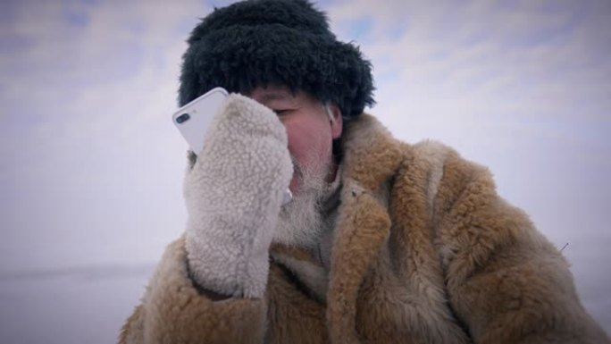 自信的土著老人坐在户外打电话，冬天风景优美，背景是天空。积极的高级蒙古人使用智能手机旅行。慢动作。