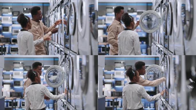 商场的游客在家电商店选择洗衣机，年轻的非洲裔配偶在交易大厅观看展览样本