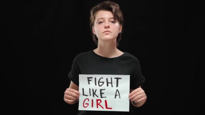 被释放的严肃的年轻女子在黑色背景下像一个女孩标志一样摆出战斗姿势。自信的高加索受虐女士为人权而战的肖