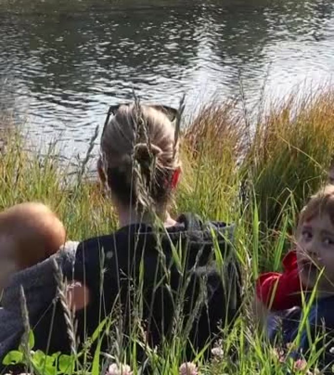 母亲和年幼的儿子在小溪边缘放松，看着鸭子