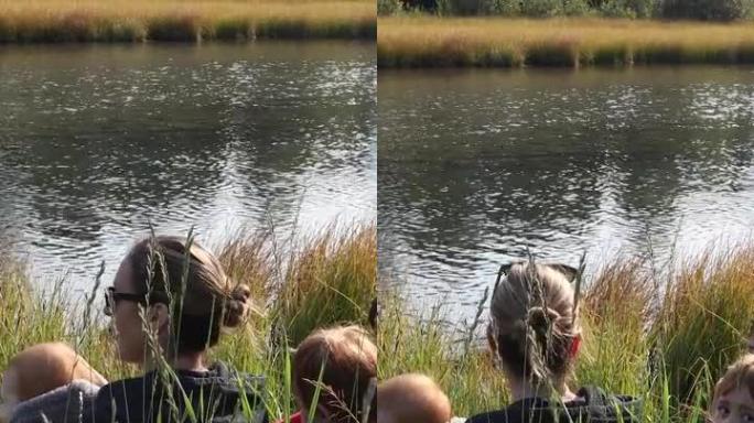 母亲和年幼的儿子在小溪边缘放松，看着鸭子