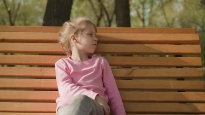 心烦意乱的小女孩坐在公园的长凳上，球迷赶走了虫子