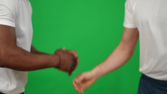 非裔美国人和高加索足球队友在绿屏上的特写高五握手。无法辨认的年轻运动员示意告别，离开chromake