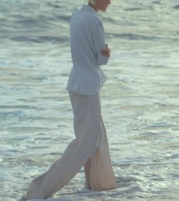 独自站在海滩上的女人。在沉思的垂直视频中眺望遥远的大海