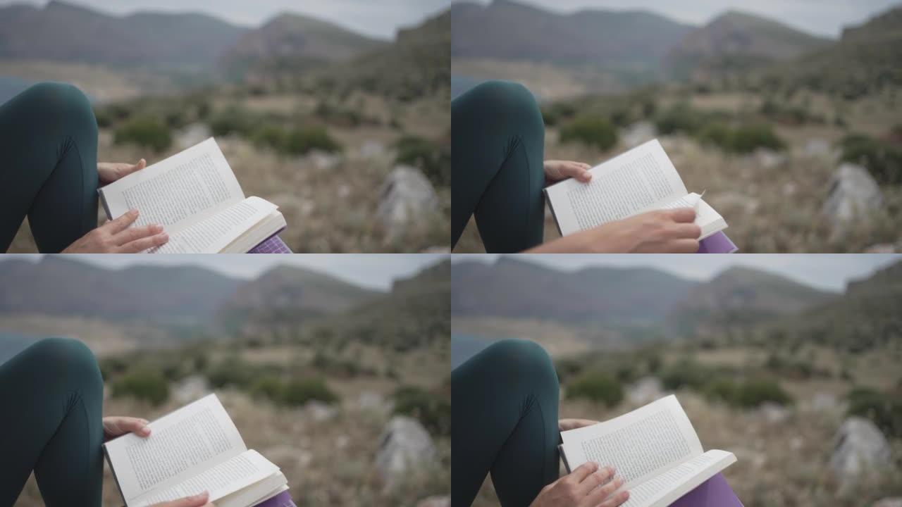 一名年轻女子在海滩附近的悬崖上读书时坐在岩石上的细节镜头