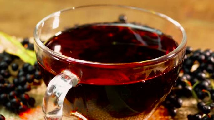 在转盘上的玻璃杯中特写天然红莓茶。黑接骨木浆果中的浆果茶。从浆果中挤出的顺势疗法果汁