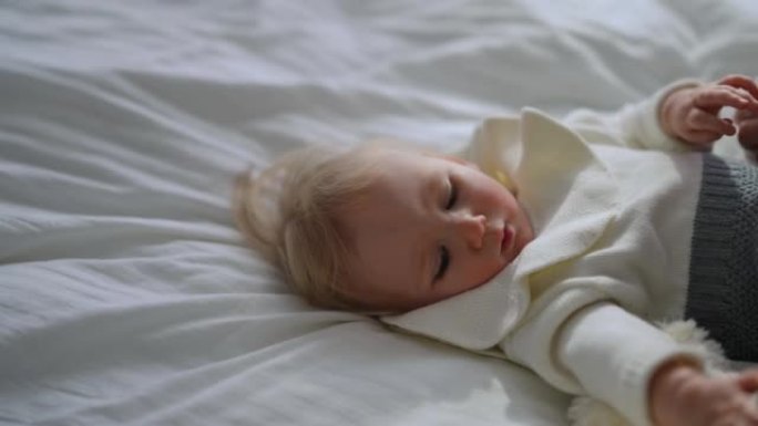 可爱的放松婴儿躺在床上的肖像，无法辨认的女人用小脚抚摸脸颊和鼻子，并以慢动作抚摸着脸。无忧无虑的高加