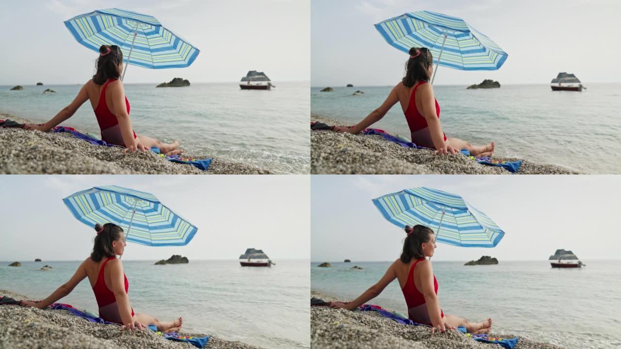 石滩上的女人在沙滩伞下放松。享受大海