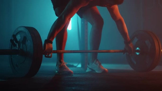 强壮的人正在黑暗的戏剧性健身房里接近杠铃，举重运动员的腿