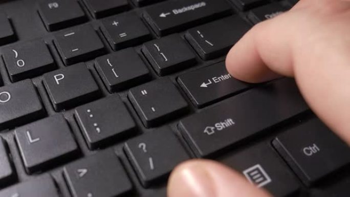 一个人的手犹豫不决，小心翼翼地按下黑色电脑键盘上的回车键，然后慢慢胆怯地松开它。特写，微距拍摄